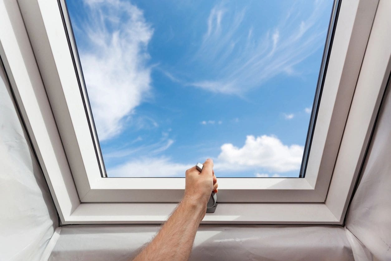 A person reaching up to look out of an open window.